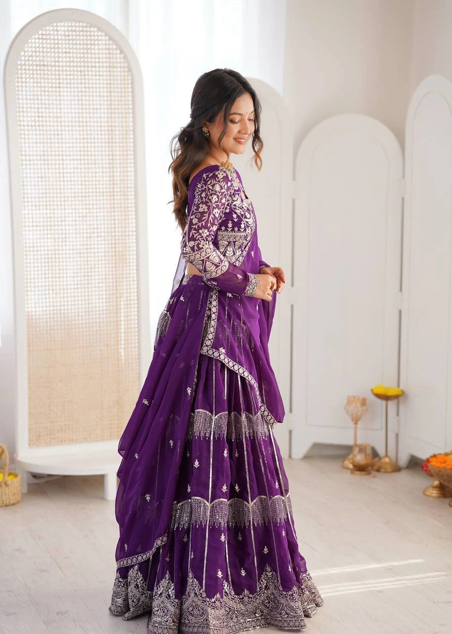 Woman in a purple and silver traditional outfit standing in a minimalistic room.
